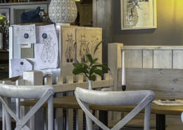 Holztisch mit zwei Stühlen und Zeichnungen von Katzen an einer Wand in einem Innenraum.