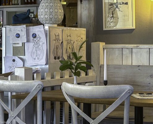 Holztisch mit zwei Stühlen und Zeichnungen von Katzen an einer Wand in einem Innenraum.
