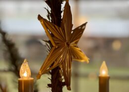 Damit die Liebe leben kann 4 Goldener Stern aus Stroh, dekoriert mit zwei leuchtenden Kerzen im Hintergrund, die eine warme Atmosphäre schaffen.