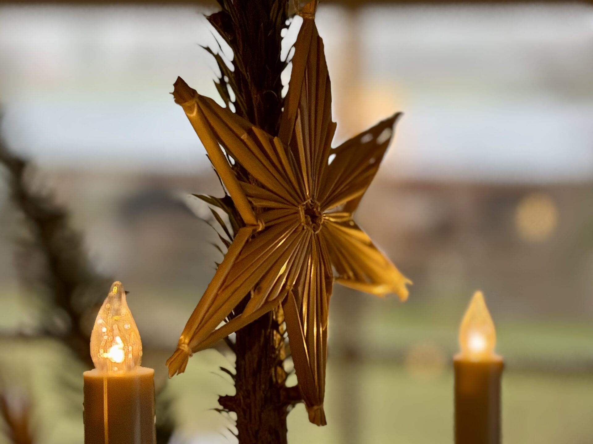 Damit die Liebe leben kann 2 Goldener Stern aus Stroh, dekoriert mit zwei leuchtenden Kerzen im Hintergrund, die eine warme Atmosphäre schaffen.