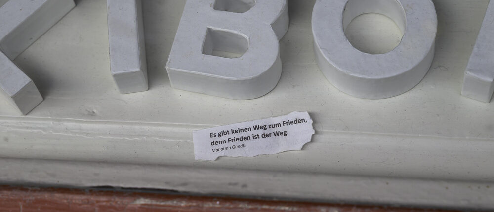 Erfurt: Weiße große 3D-Buchstaben liegen auf einem roten Sockel; darunter klebt ein Zitat von Mahatma Gandhi über Frieden, Blickfang durch Kontrast von Weiß und Rot